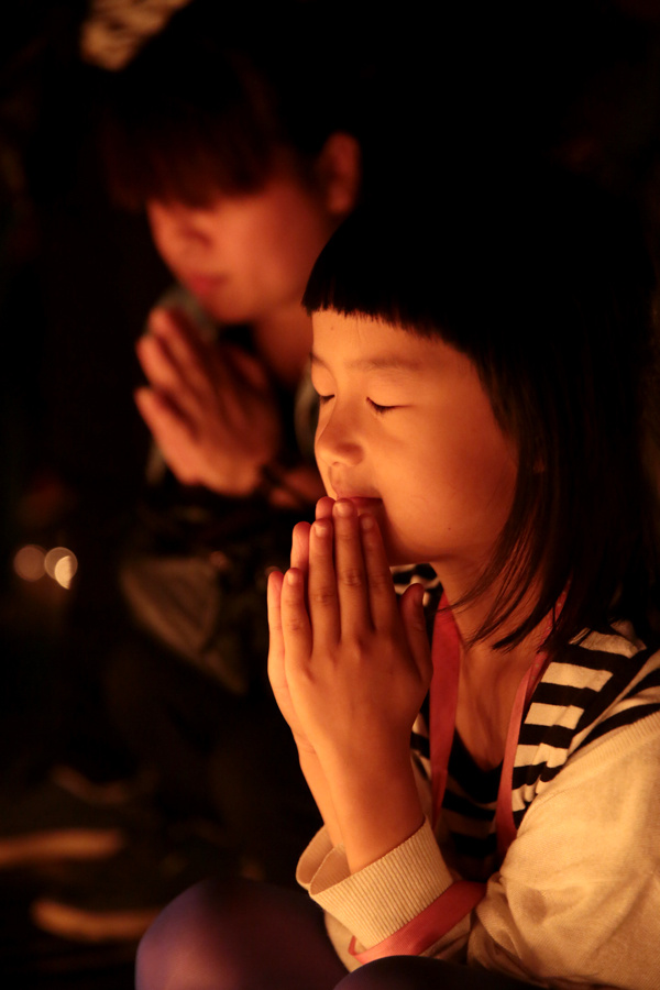 图为一名当地的小女孩随着家人来到祈福现场,并双手合十